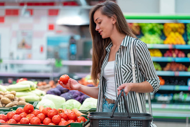 Woman chooses fresh ripe tomatoes in vegetable department of supermarket. Customer buying food at grocery store - Фото, зображення