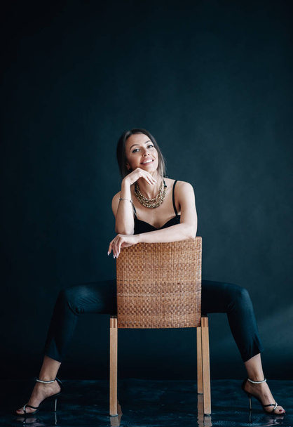 Beautiful woman sits on chair and looks into the camera - Фото, зображення
