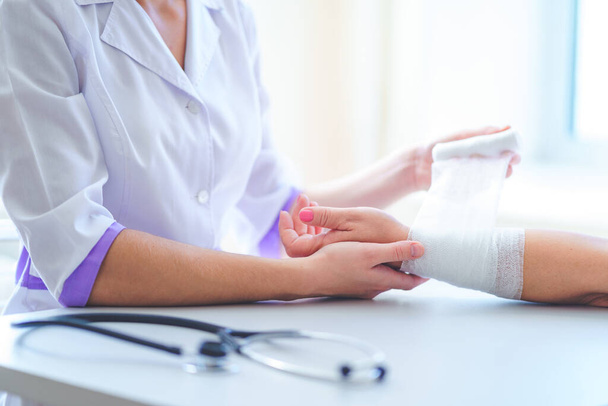 General practitioner bandages wrist of patient in hospital  - Фото, изображение
