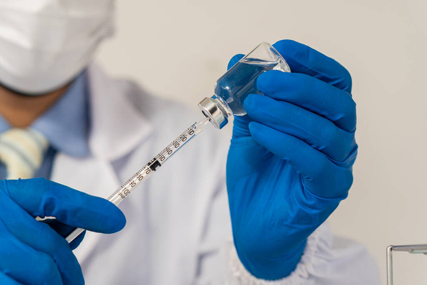 γιατρός, επιστήμονας με μπλε γάντια, κρατώντας ένα μπουκάλι εμβόλιο covid-19, προετοιμάζοντας παιδιά και ενήλικες για τον εμβολιασμό ανδρών και γυναικών. Η έννοια της θεραπείας της γρίπης, ασθένεια του ιού του στέμματος - Φωτογραφία, εικόνα