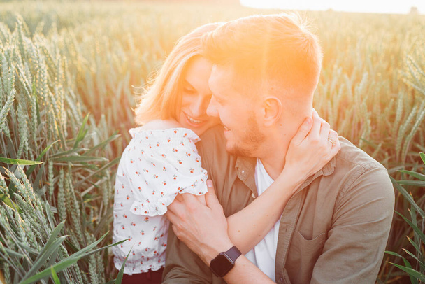 Szczęśliwa młoda para obejmuje, siedząc w wysokiej trawie na polu w promieniach zachodzącego letniego słońca. Miłość i czułość. Piękne chwile życia. Młodość i piękno. Pokój i nieostrożność.  - Zdjęcie, obraz
