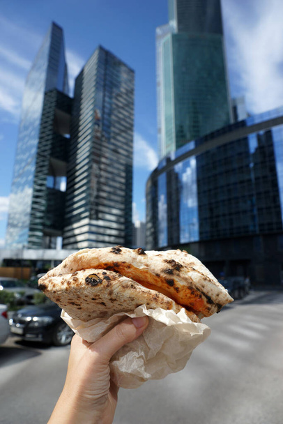 pizza napolitaine roulée comme un portefeuille à la main sur fond de gratte-ciel modernes. - Photo, image