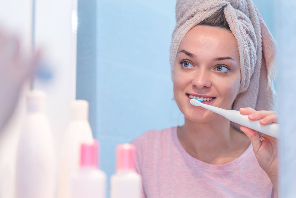 Happy attractive healthy woman brush teeth using ultrasonic electric toothbrush in bathroom at home. Oral hygiene, dental and gum health, healthy teeth. Daily life and routine - Foto, imagen