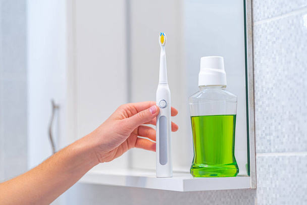 Ultrasonic electric toothbrush with interchangeable nozzles and mouthwash for fresh breath in bathroom at home. Oral hygiene, dental and gum health, healthy teeth. Dental products  - Zdjęcie, obraz
