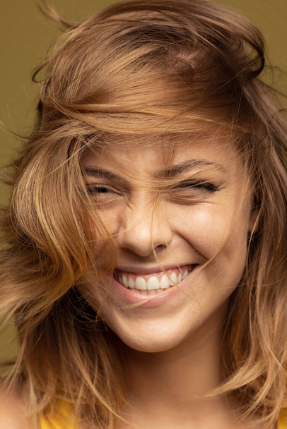 Close-up portrait of young happy smiling caucasian woman on dark yellow background. - Foto, afbeelding