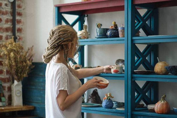 hostess of the ceramic workshop lays out her ceramic dishes on the shelves. feng shui concept. Small business office - Fotoğraf, Görsel