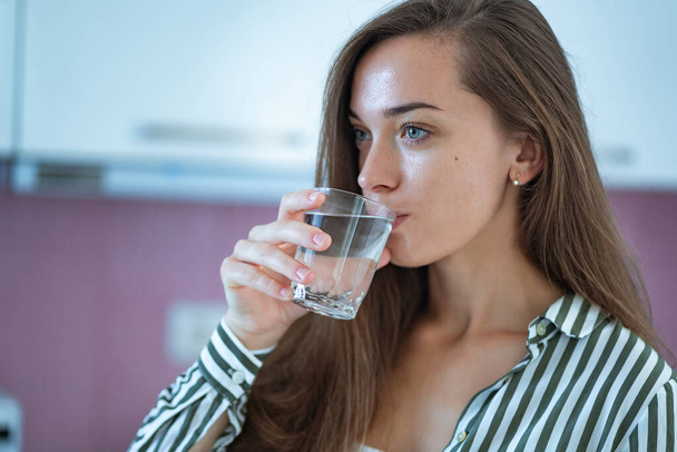 Happy attractive young woman drinks clear purified glass of water in the kitchen at home. Healthy lifestyle - Fotografie, Obrázek