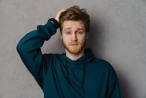 Bearded ginger man holding his head and looking at camera isolated over grey background - Foto, Imagem