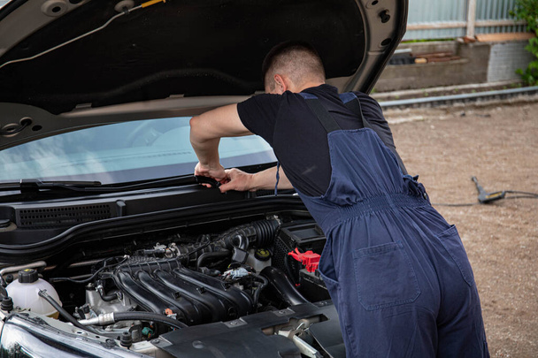 a man repairs a car. a man in blue special clothes to repair the car. engine parts machine repair maintenance breakage problem hands people man master - Photo, Image