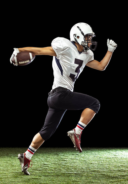 Portrait of American football player training isolated on dark studio background with grass flooring. Concept of sport, competition, goals, achievements - Foto, Bild