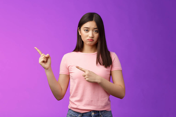 Moody upset whining girlfriend unhappy pointing left, sulking look miserable and distressed, express regret and disappointment, complain bad fortune, stand purple background displeased - Foto, Imagen