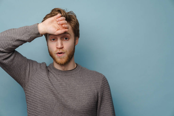 White ginger man looking at camera while wiping his forehead isolated over blue background - Foto, Bild