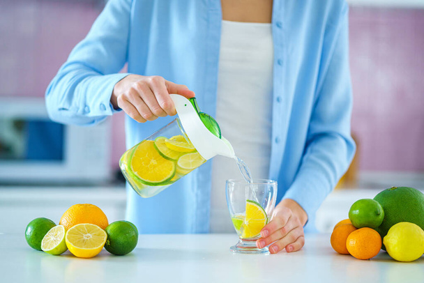 Woman pouring refreshing infused detoxification citrus water from jug in a glass for vitamin detox drink. Slimming antioxidant drinks for diet healthy drinking  - Photo, image