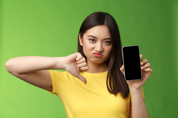 Close-up rozczarowany zdenerwowany azjatyckie dziewczyna sądząc zła okropna aplikacja, pokaż ekran smartfona, kciuk w dół grymaszenie niezadowolony, dać negatywne opinie, nie może znieść ex-chłopak nowa dziewczyna - Zdjęcie, obraz