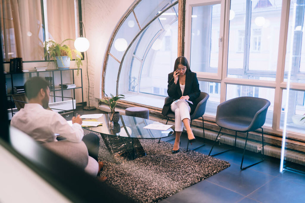 Επιχειρηματικοί εταίροι συζητούν για το έργο στο smartphone και κρατώντας σημειώσεις, ενώ κάθεται στην άνετη αίθουσα με μοντέρνα έπιπλα και φωτεινό φωτισμό - Φωτογραφία, εικόνα