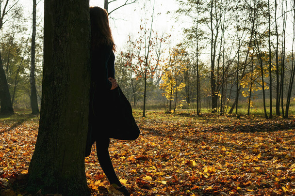 A young girl in a yellow jacket walks in an autumn park with fallen leaves - Foto, immagini