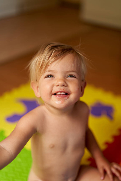 Riendo niño pequeño con una cara sucia se sienta en el suelo en la habitación - Foto, imagen