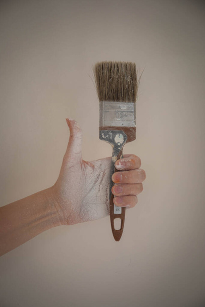 la mano de una mujer con un pincel untado con pintura. una mujer pinta las paredes con pintura blanca. manchado a mano en pintura blanca pintor de pared pincel - Foto, imagen
