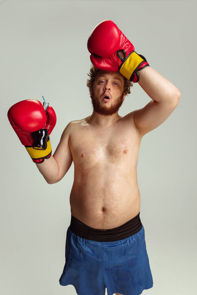 Funny red-headed man in blue boxing shorts and gloves isolated on gray studio background. Concept of sport, humor and body positive. - Foto, Imagem
