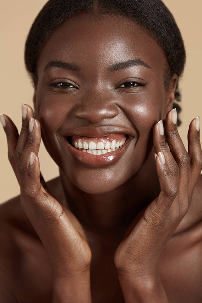 Portrait close up of beautiful african girl. Smiling young woman touch her clean face and looking at camera. Concept of face skin care. Isolated on beige background. Studio shoot - Foto, Bild