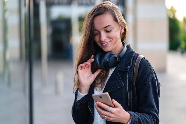 Stylish casual fashionable happy hipster woman teen with wireless headphones while walking around the city. Lover music enjoying music  - Valokuva, kuva