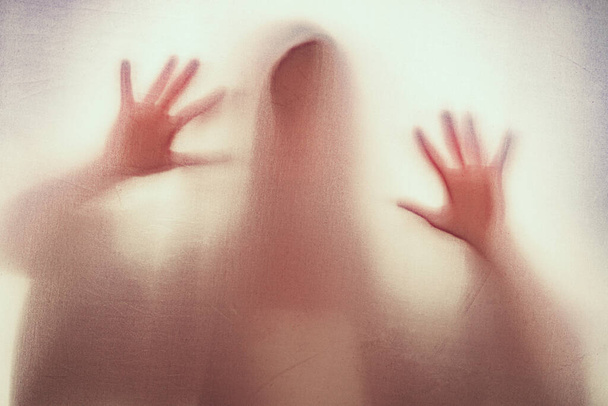 Shadow of scary paranormal ghost horror woman behind the matte red glass in soft focus. Blurry hand and body figure abstraction. - Foto, immagini