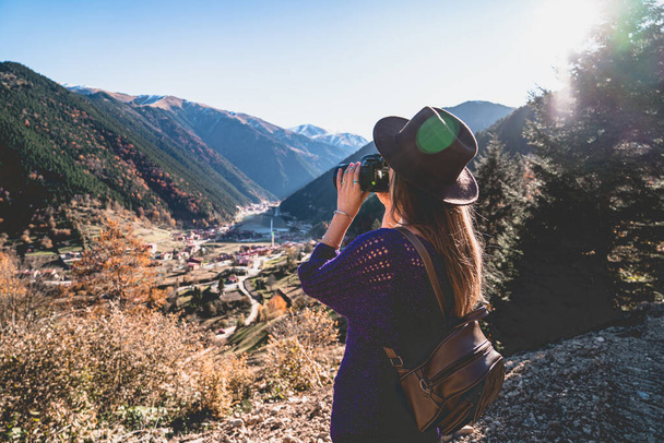 Stylish trendy hipster woman traveler photographer in a felt hat with brown backpack taking pictures of the mountains and uzungol lake in Trabzon during Turkey travel  - Photo, image