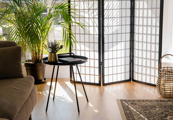 Главная гостиная с деревянным и бумажным разделителем экран блокирующий солнце от окна, черный металлический стол акцент и диван, натуральные цвета. - Фото, изображение