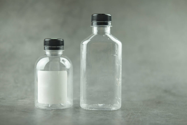 Empty bottle of transparent plastic with black lids on a black background - Foto, afbeelding