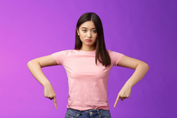Serious-looking upset insecure asian female fighting stop cruel animal behaviour, pointing fingers down disappointed, look camera sincere fed up, standing depressed unsatisfied, purple background - Photo, Image