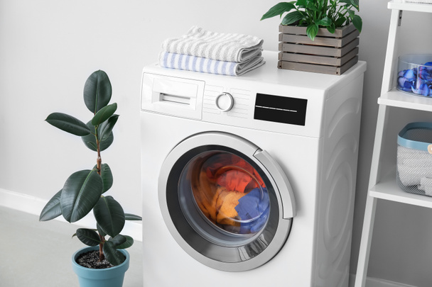 Çamaşırları ve ışık duvarının yanında bitkileri olan modern çamaşır makinesi. - Fotoğraf, Görsel