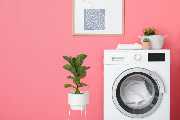 Modern washing machine with laundry and houseplants near color wall - Fotó, kép