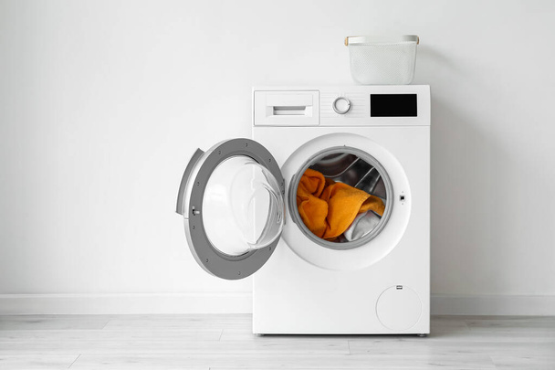 Moderne Waschmaschine mit Wäsche in der Nähe der Lichtwand - Foto, Bild
