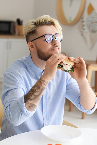 Young man eating vegan burger in kitchen - Photo, Image