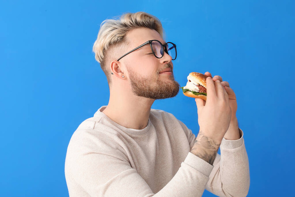 Young man eating vegan burger on color background - Zdjęcie, obraz