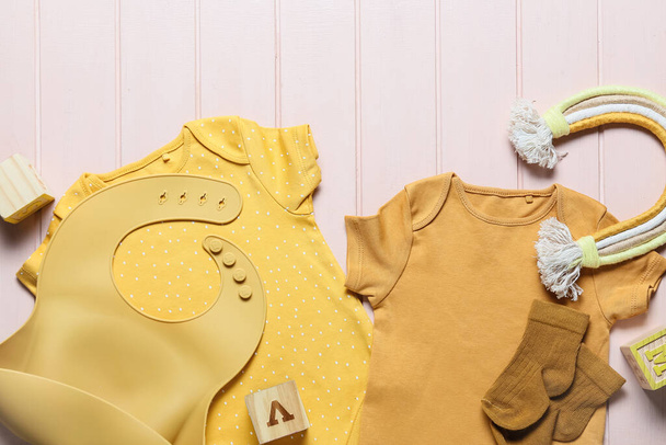 Ubrania dla niemowląt, śliniak i zabawka na kolorowym drewnianym tle, zbliżenie - Zdjęcie, obraz