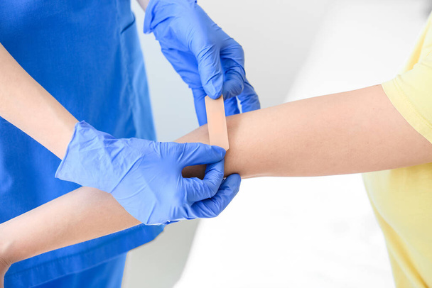 Verpleegster brengt medische pleisters aan op de arm van een jonge vrouw in de kliniek - Foto, afbeelding