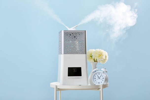 Modern humidifier, vase and alarm clock on table against color background - Φωτογραφία, εικόνα