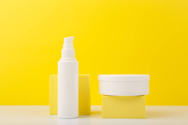 Face cream and body cream in white tubes with geometric props against yellow background. Concept of beauty products for face and body care - Φωτογραφία, εικόνα