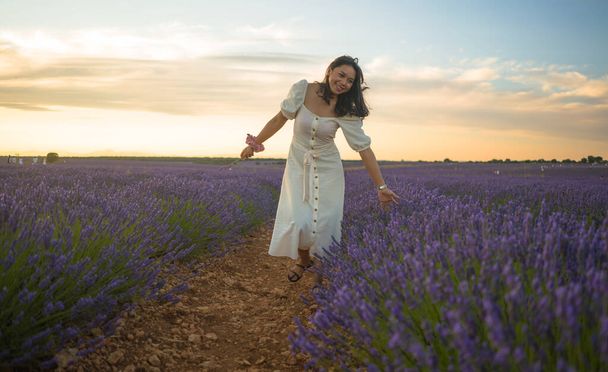 outdoors romantic portrait of young happy and attractive woman in white summer dress enjoying carefree at beautiful lavender flowers field in travel and holiday concept - Fotó, kép