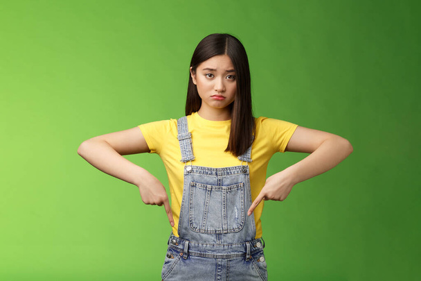 Sad asian girl in dispair feel upset, frowning sulking pessimistic, pointing down look camera pulling sorrow uneasy face, express sadness and frustration, stand green background - Photo, Image
