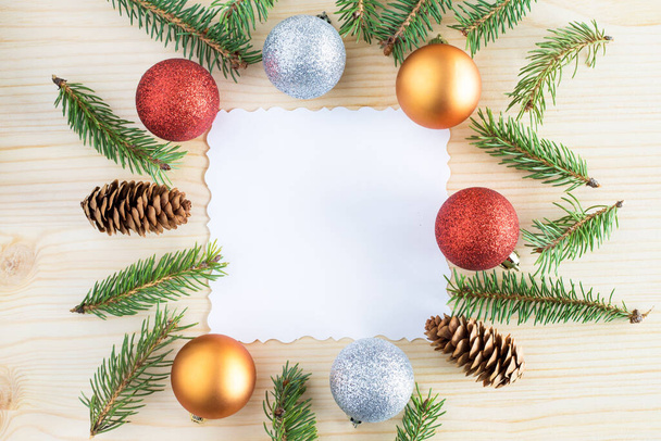 Weihnachtsrahmen Hintergrund mit Weihnachtsdekoration aus Tannenzweigen, Zapfen und Kugeln um leeres weißes Papier für Text. Kopierraum in der Mitte - Foto, Bild