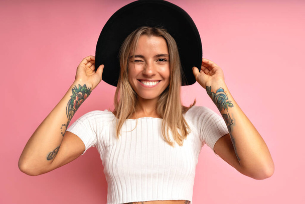 Stylish young positive woman having fun, wearing trendy casual clothes and hat. Indoor studio portrait at pink background, copy space. - Фото, зображення