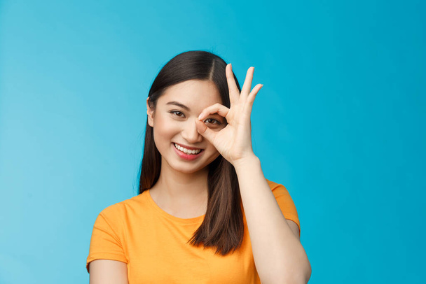 Close-up aranyos álmodozó érzékeny ázsiai nő sötét rövid frizura show oké ok jel nézd át a kört mosolyogva széles körben, kifejezni pozitivitás jó hangulat, álló vidám barátságos tekintet kamera, kék háttér - Fotó, kép