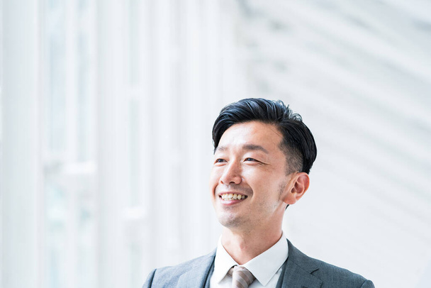 Asian businessman smiling in a bright indoor space - Photo, Image