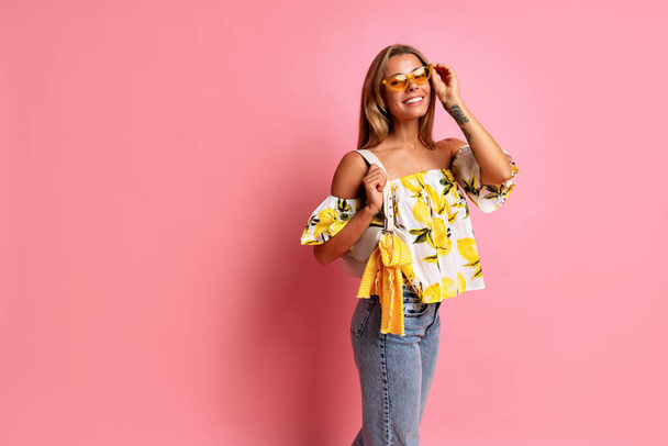 Fashionable portrait of  young blogger woman wearing top with lemon print posing at studio pink background, travel positive mood, Italian fashion style. Summer trendy outfit and accessorizes.  - 写真・画像