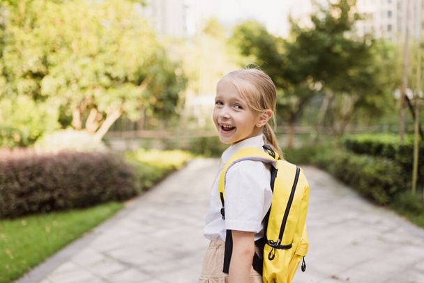 Η μαθήτρια επιστρέφει στο σχολείο μετά τις καλοκαιρινές διακοπές. Μαθητής με στολή χαμογελά νωρίς το πρωί εξωτερική.  - Φωτογραφία, εικόνα