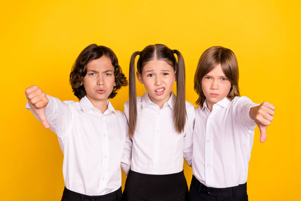 Photo of three upset frustrated schoolchildren show thumb down wear white shirt isolated yellow color background - Foto, imagen