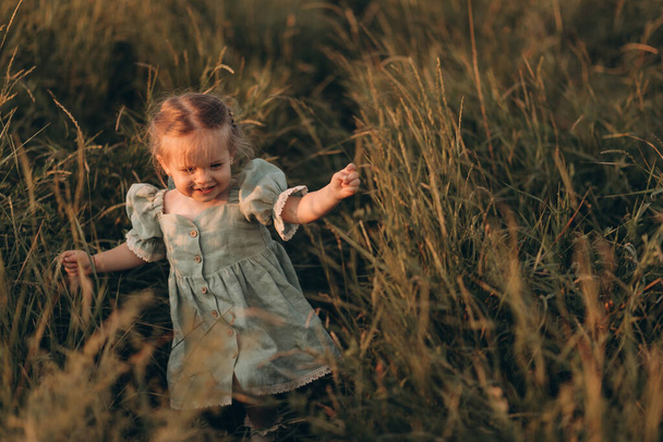 Caucasian little girl in a dress walks in the park in the rays of the setting sun - Photo, image