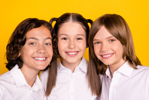 Photo of three cheerful kids look camera shiny white smile wear white shirt isolated yellow color background - Foto, Imagen